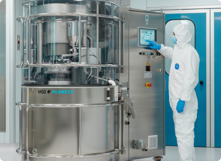 An operator in protective gear operating an MG2 pharmaceutical capsule filling machine inside a clean room.